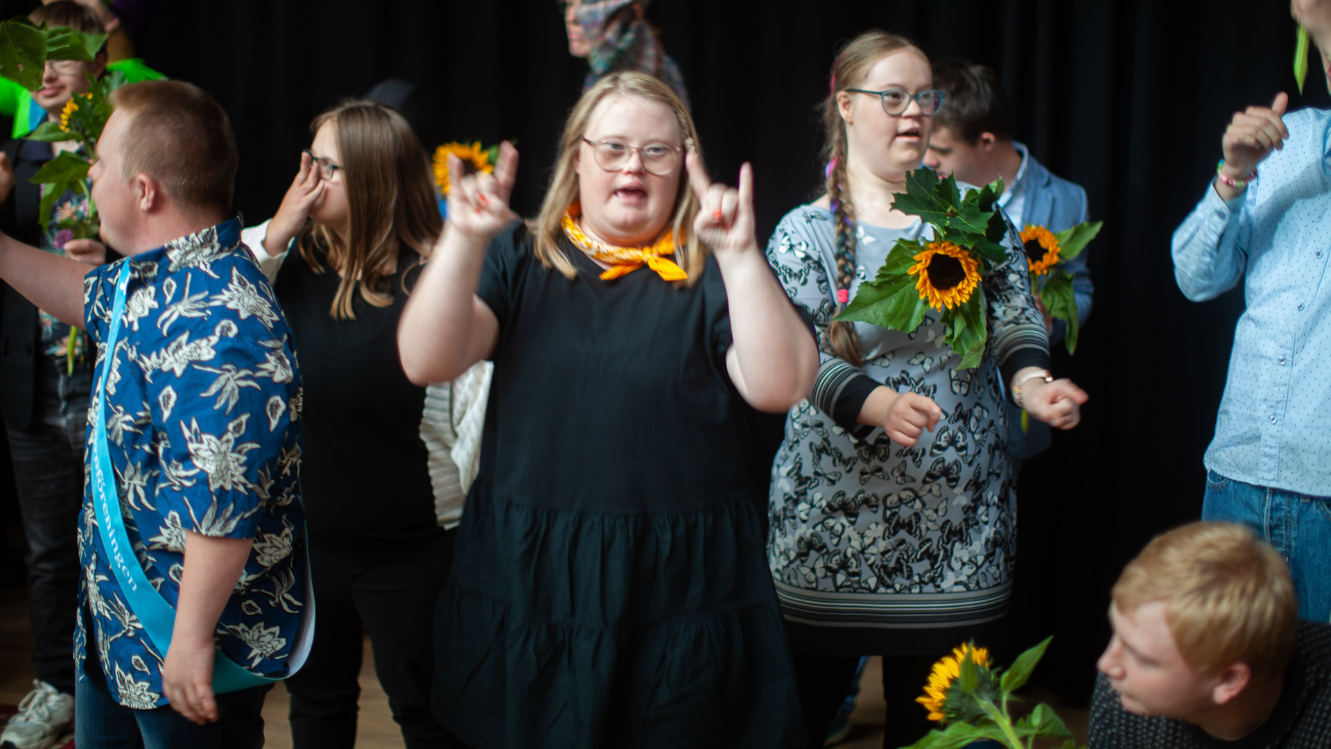 Bild från jubileumsfirandet på Världskulturmuseet. Flera personer med Downs syndrom står på scen och sjunger och tecknar Rocka sockorna låten